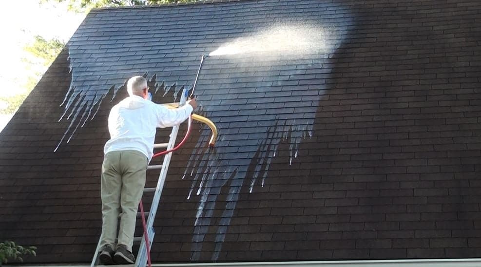 A man on a ladder spraying a roof.